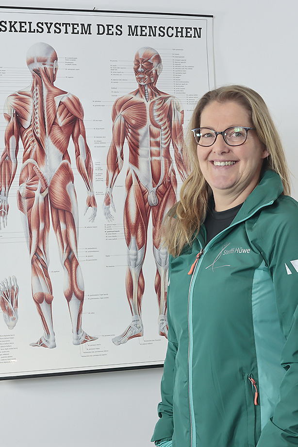 Steffi Hüwe steht vor einem Plakat mit dem Muskelsystem des Menschen